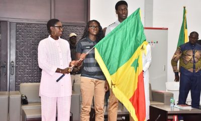 Three people on a stage; a flag with green, yellow, and red is being held aloft during a formal ceremony.