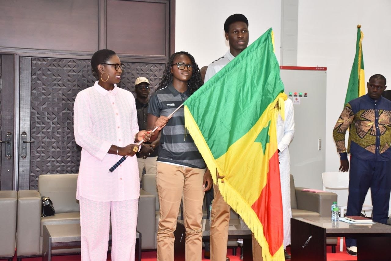 Three people on a stage; a flag with green, yellow, and red is being held aloft during a formal ceremony.