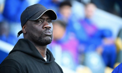 Man in a black hoodie and cap stands in a stadium, looking off to the side with a focused expression.