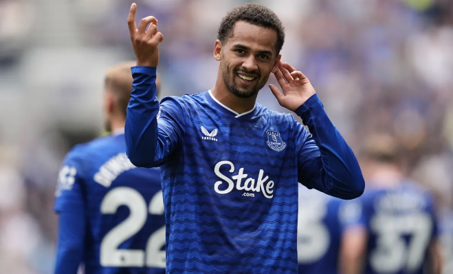 Soccer player in a blue jersey waving and smiling on the field