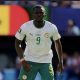 Soccer player wearing white jersey with green accents and number 9, on the field for Senegal.