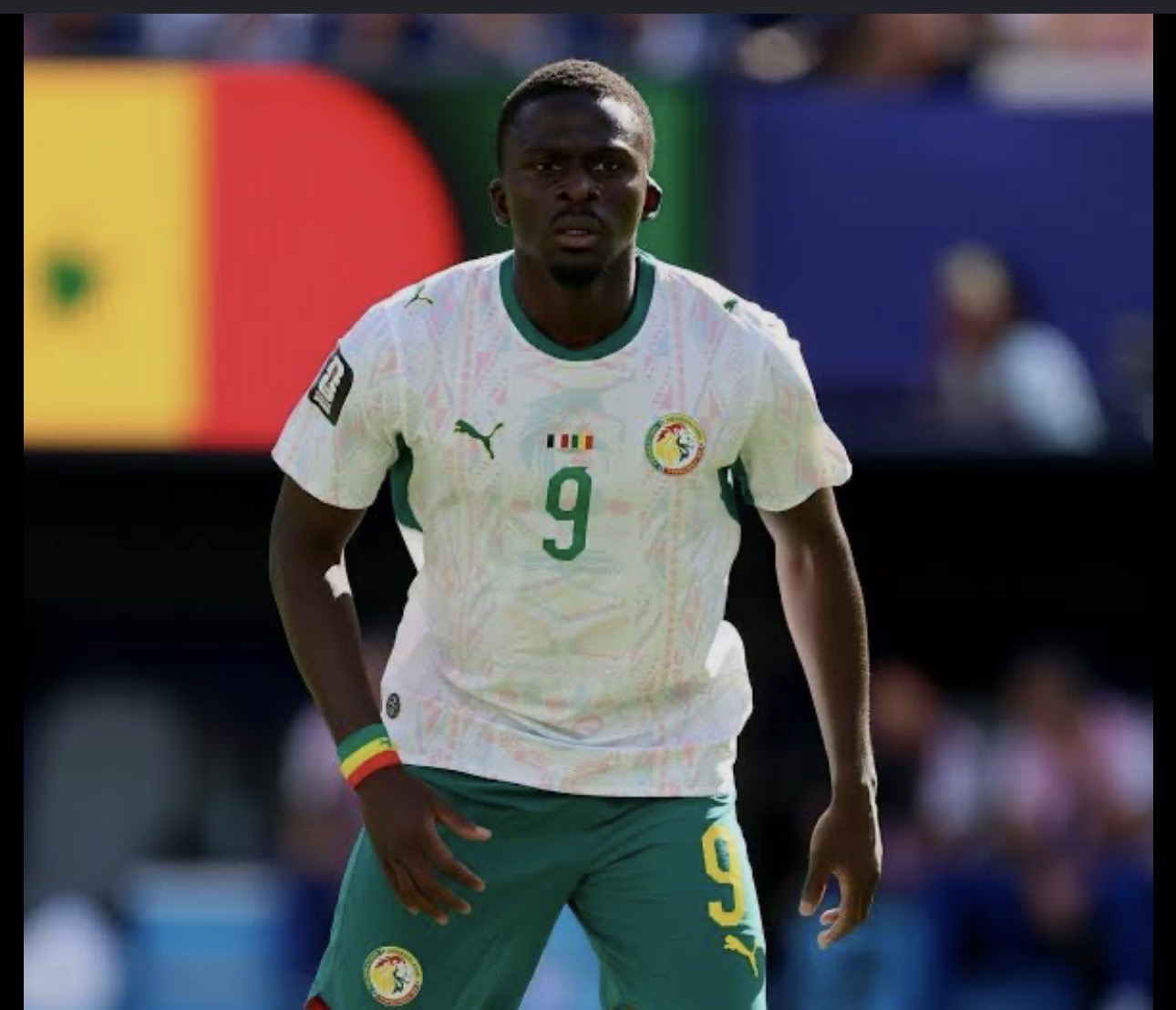 Soccer player wearing white jersey with green accents and number 9, on the field for Senegal.