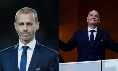 Two men in dark suits at a formal event; the left man has a short gray beard and the right man is bald with arms raised on a stage.
